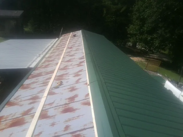 Old rusted panels beside newly installed green metal roofing — Wind Damage Roof Repair by Roofing Brothers in Gold Bar