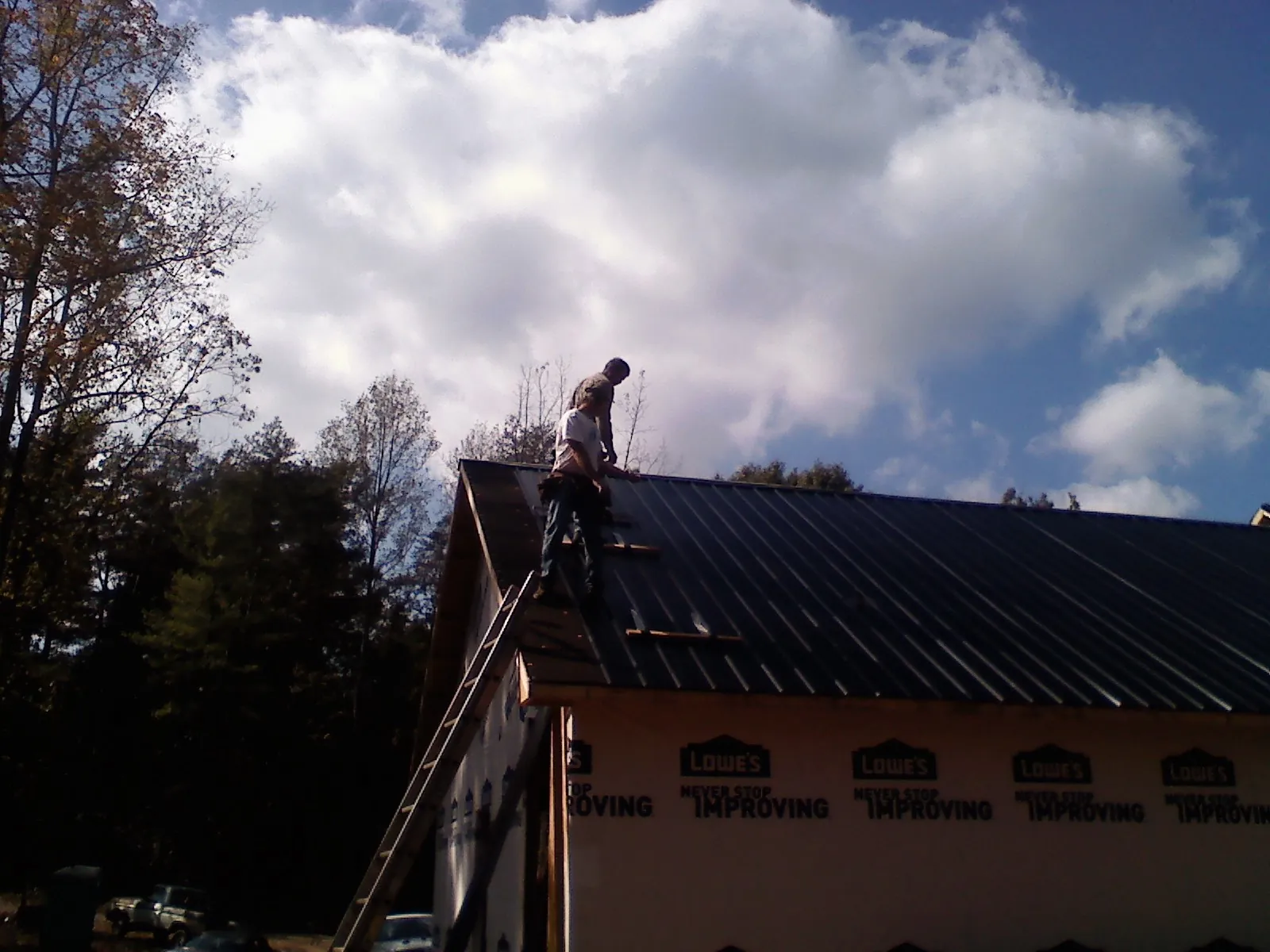 Roofer fastening dark metal panels high against a cloudy sky, from a Roof Inspection job in Gold Bar