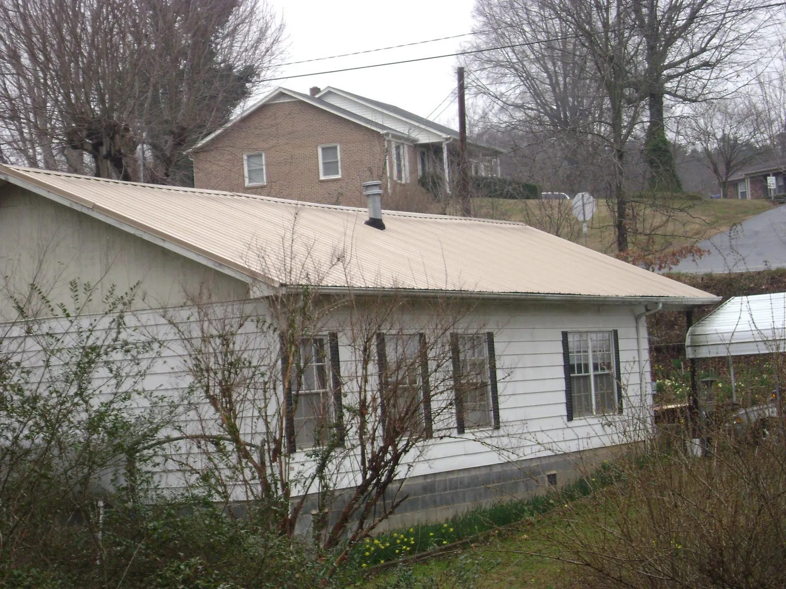 Tan metal roof on a white sided house set into a hillside — Commercial Roofing by Roofing Brothers in Gold Bar